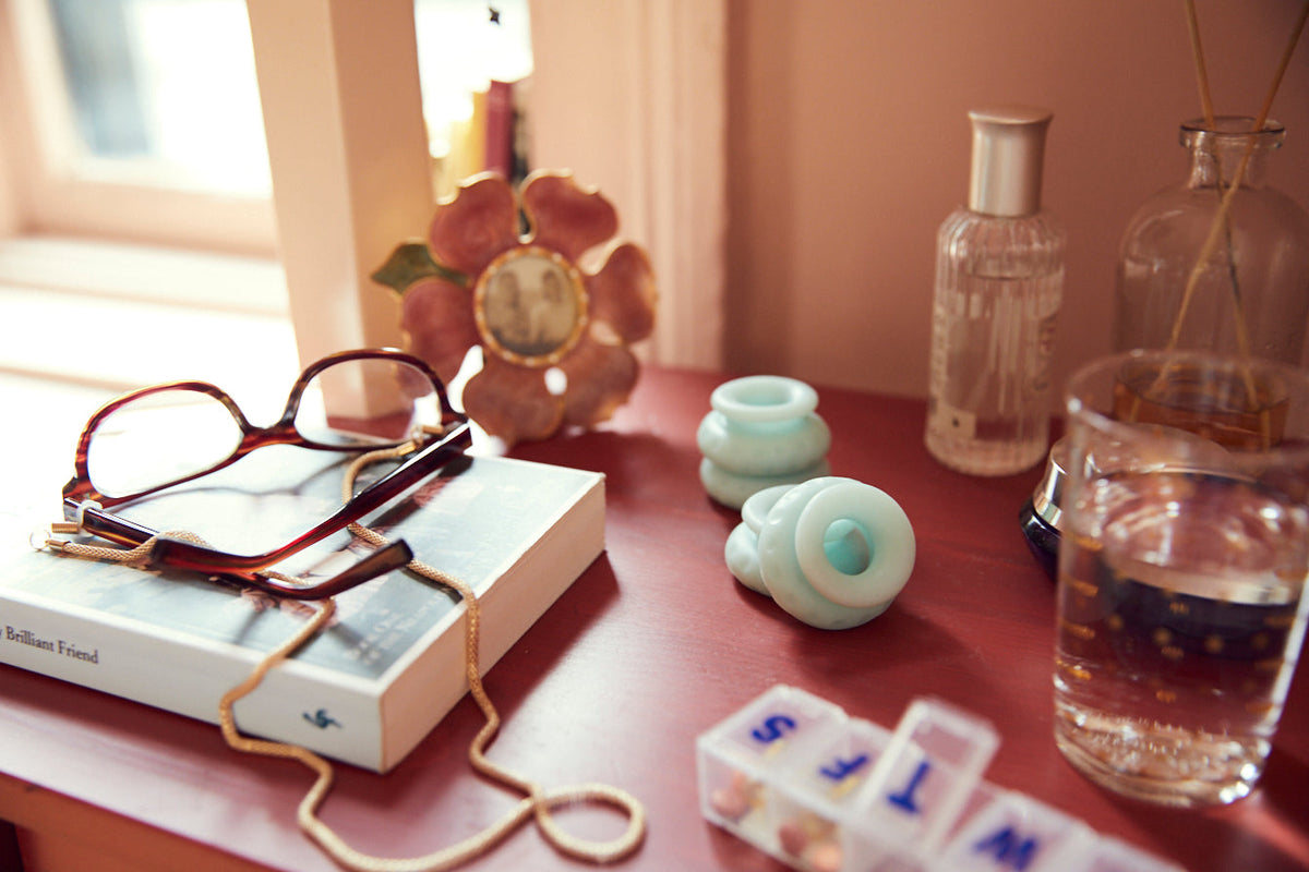 A shot of a nightstand with a picture frame, book, glasses, glass of water,  Ohnut and a pillbox