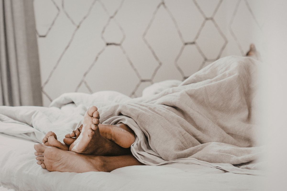 Feet of two people intertwined underneath a blanket