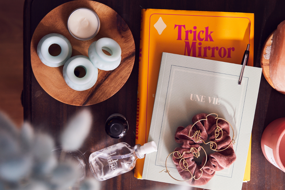 An overhead shot of someone's nightstand with books, a journal , a candle and Ohnut.