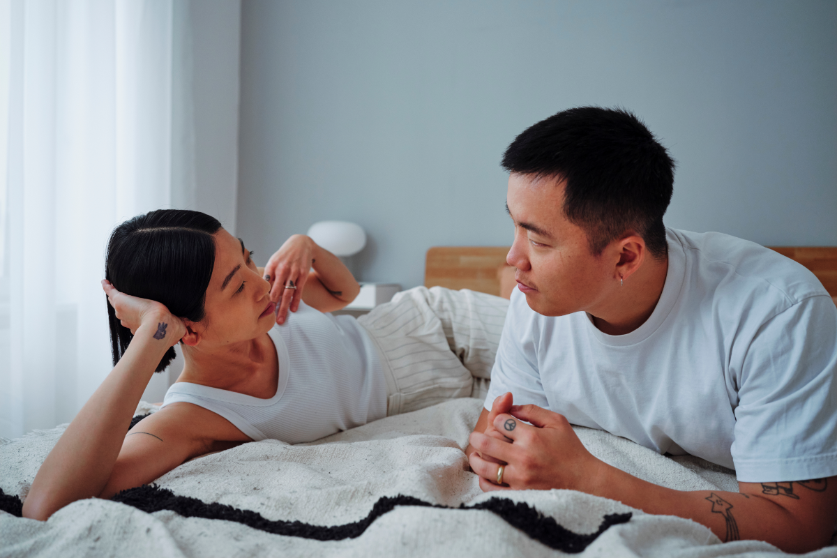 A couple has a serious, supportive conversation laying on the bed.