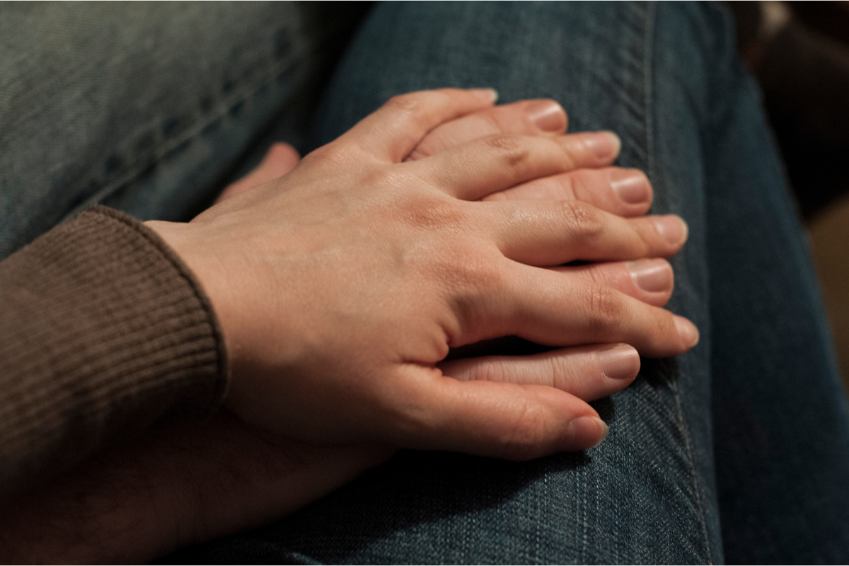 Two hands intertwined resting on someone's leg
